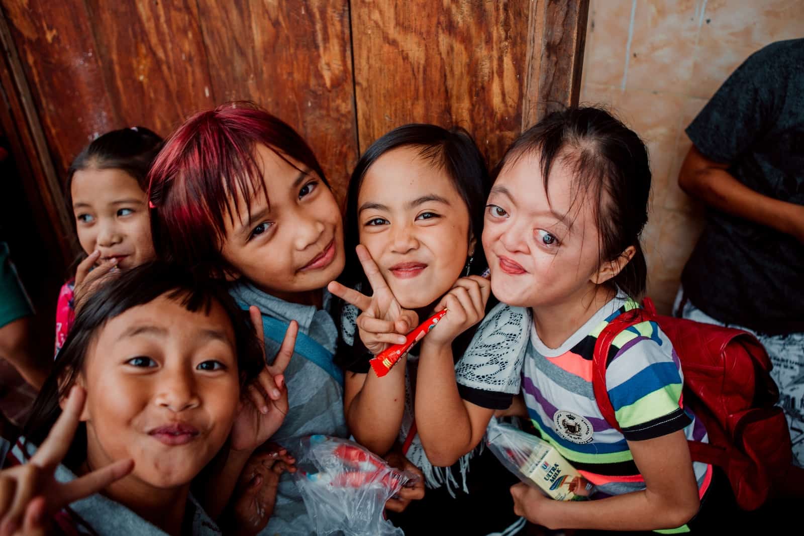 Four young girls, including one with Apert Syndrome, smile at the camera, making peace signs.
