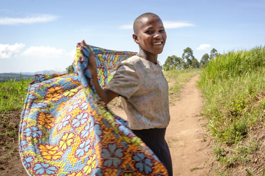 A girl holds a floral scarf, blowing behind her, while she turns and smiles at the camera.