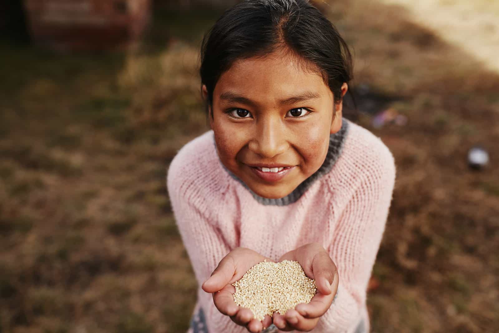 A girl in a pink sweater holds up a handful of seeds.