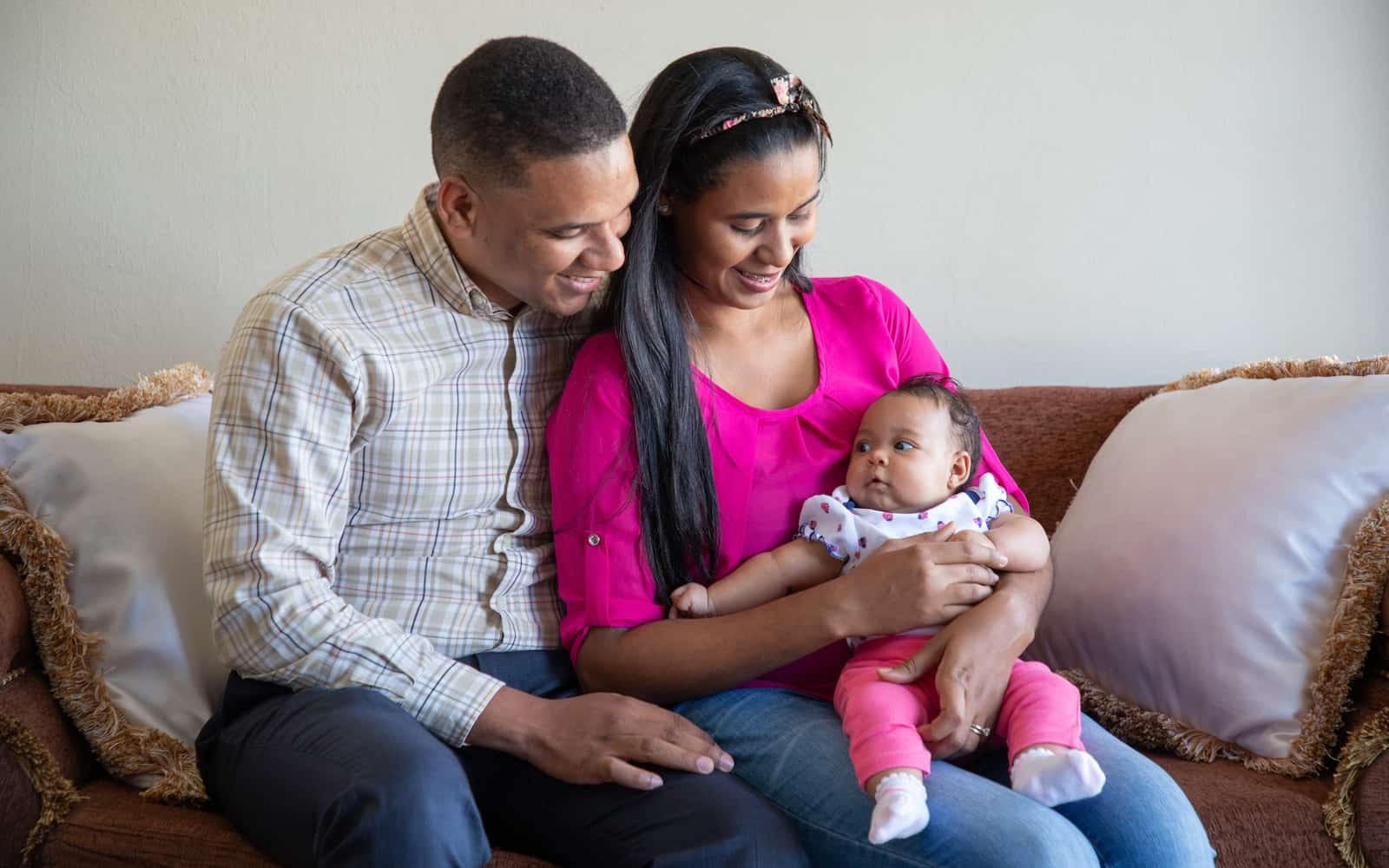 A man and woman sit on a couch, holding a baby. 