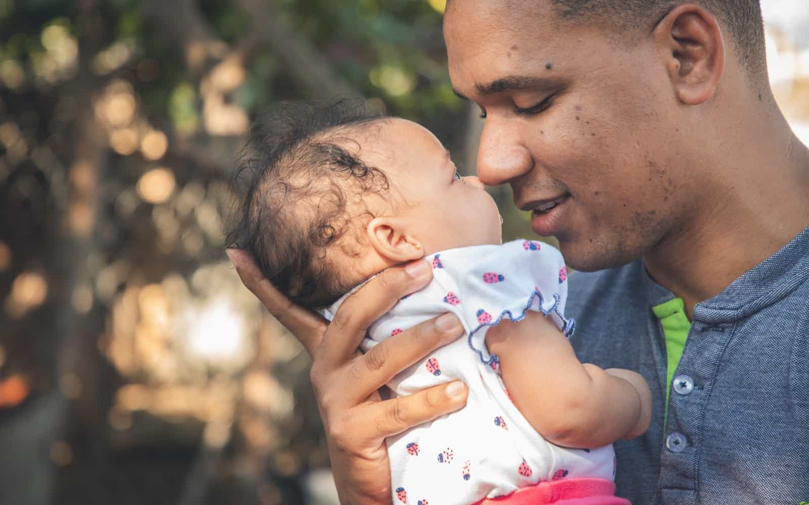 A man holds a baby up to his face, smiling.