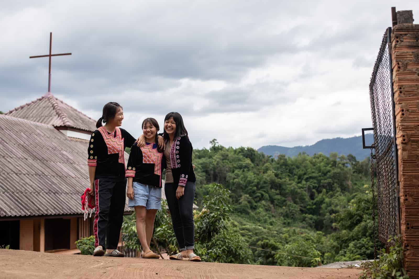 Three girls stand on the road in front of a church in a rural area. 