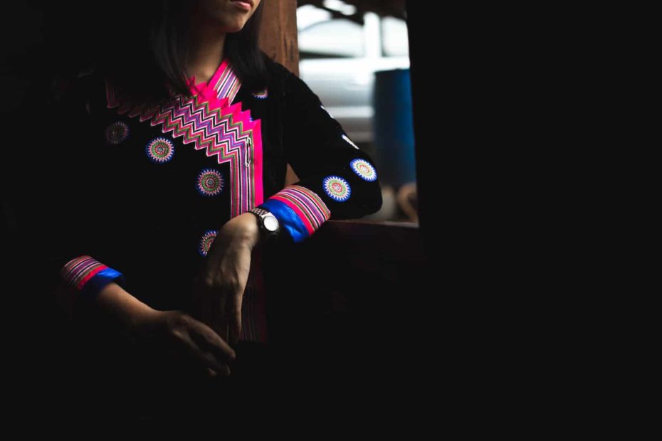 A girl wearing a colorful traditional Hmong outfit looks out the window.