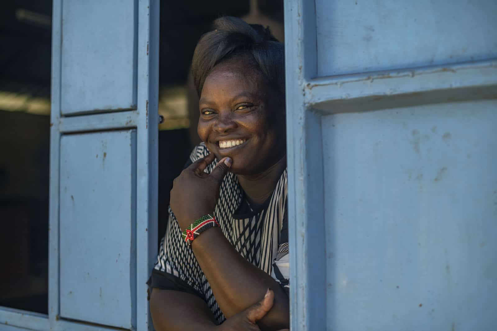 A woman who is a crusader against FGM leans out of a window with blue shutters. 
