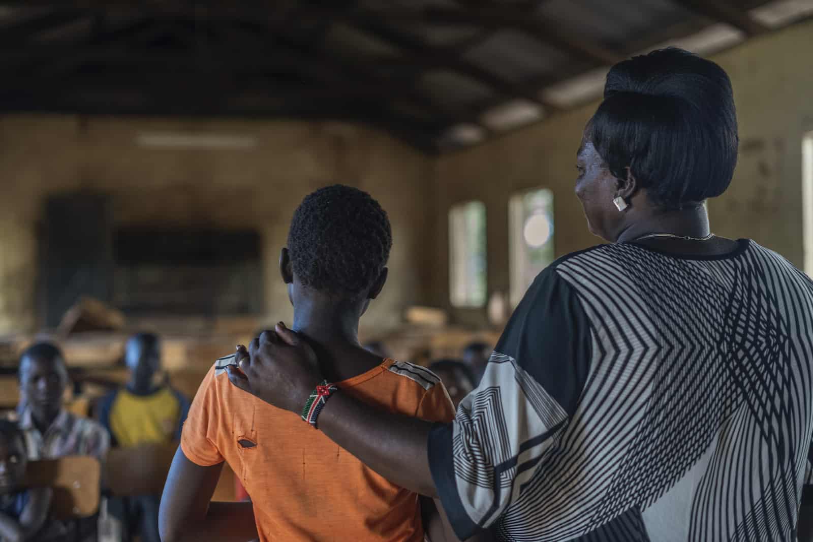 A picture from behind of a woman standing with her arm around a girl.