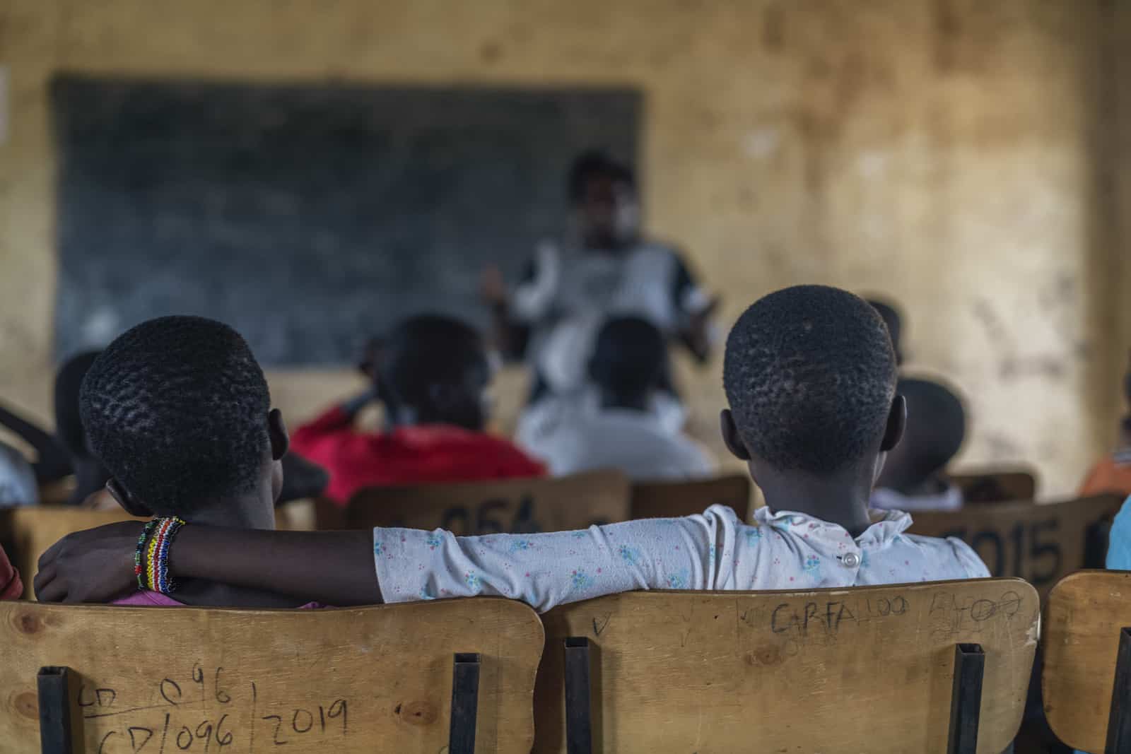 Children sit in a school for girls who have escaped FGM, listening to a woman standing in front of the class.