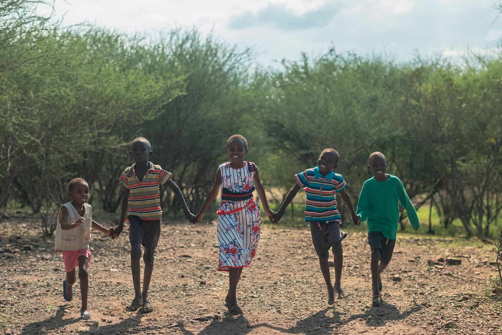 A group of five children hold hands and run towards the camera.