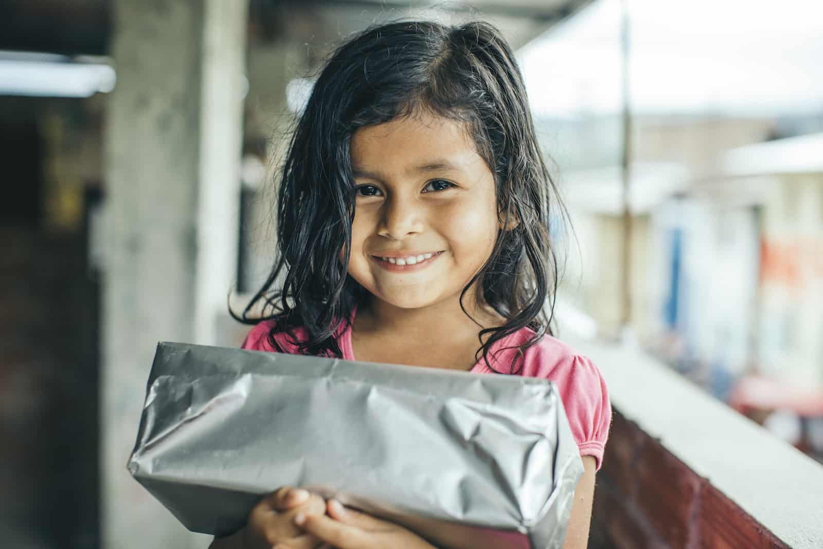 A girl in a pink shirt holds a silver present.