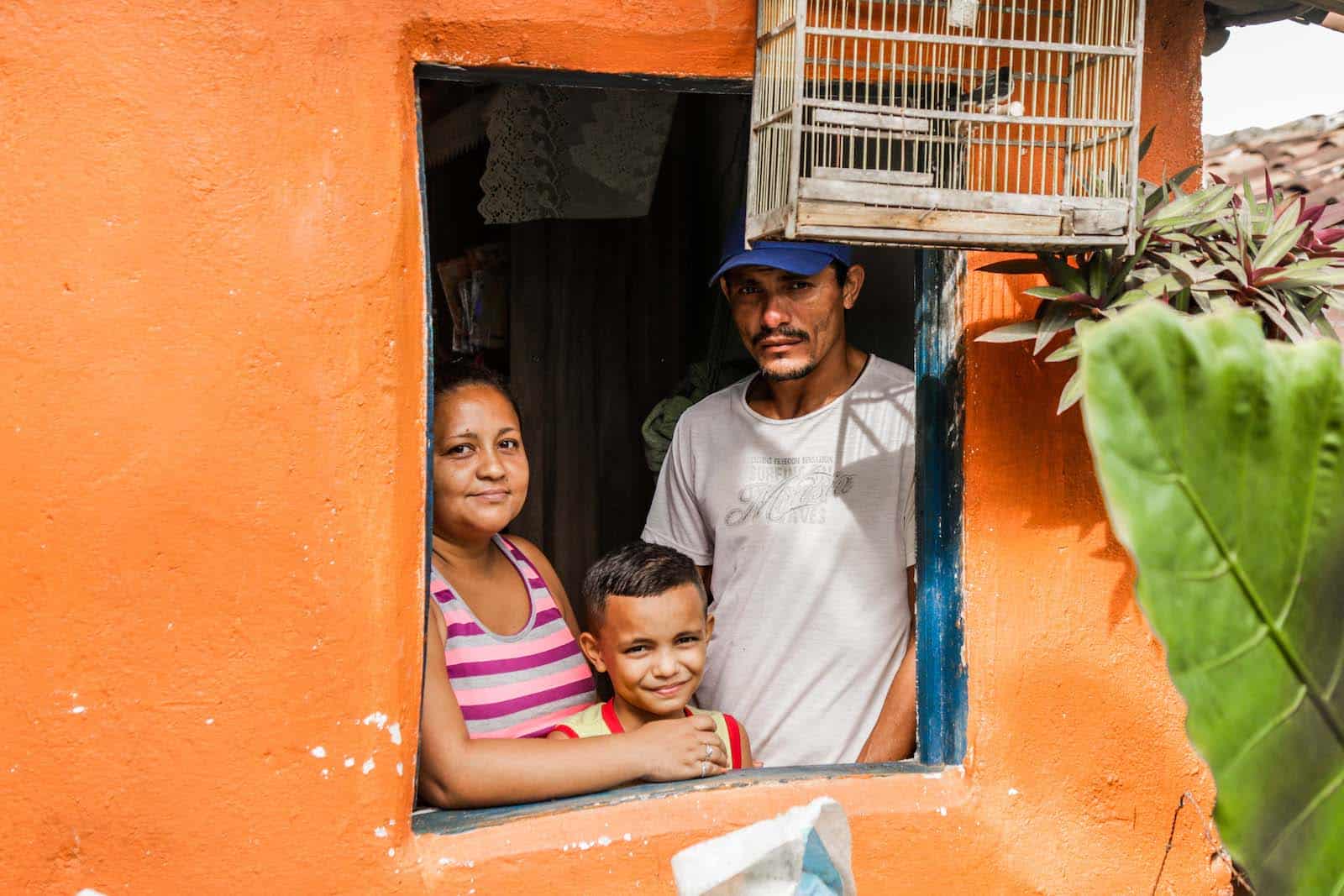 A man, woman and child stand looking out a window of an orange building.