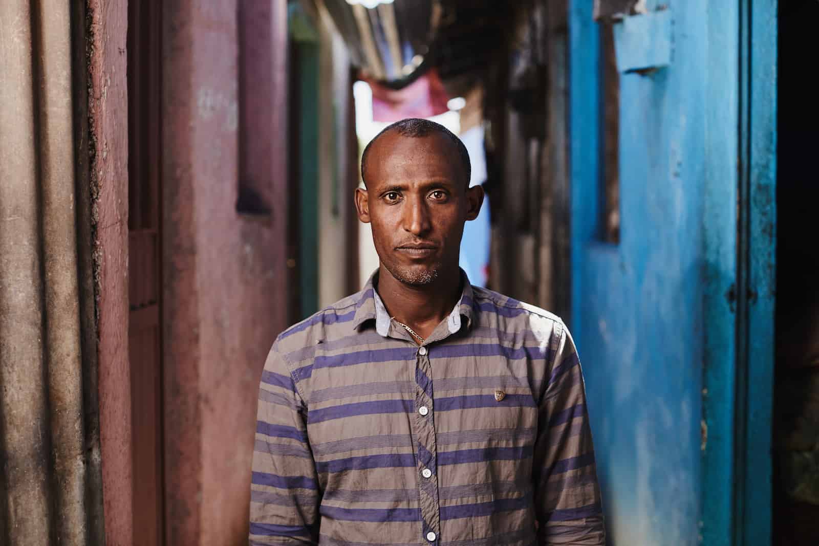 A man stands in a narrow alleyway with pink and blue walls. 