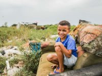 A boy sits on an old sofa in a garbage dump.