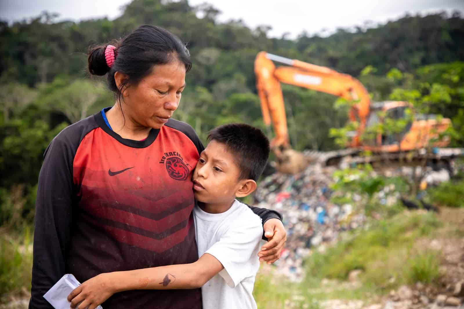 A woman and son stand in front of a large piece of machinery at a landfill. 