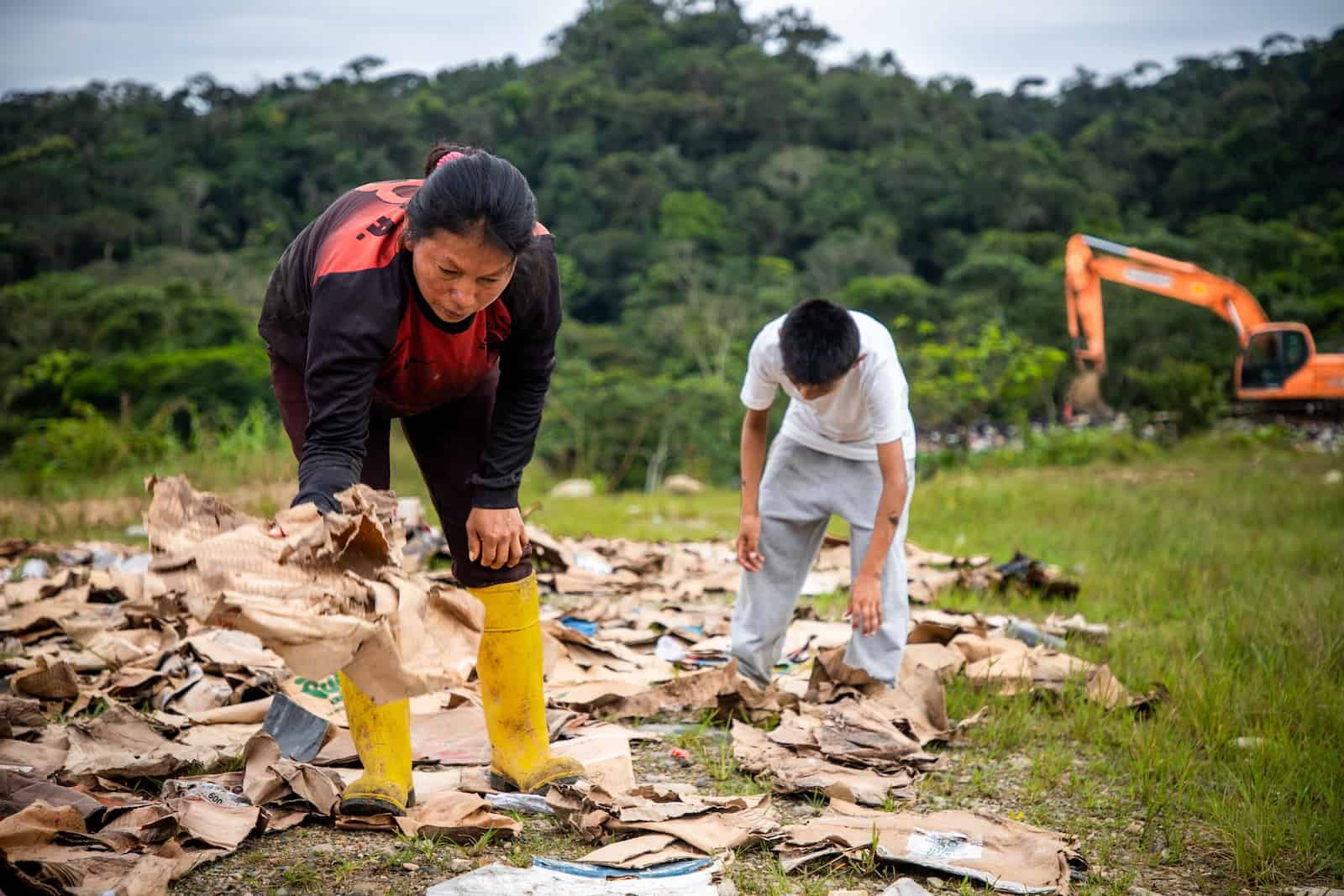 A woman and boy lean over a landfill, sorting cardboard.