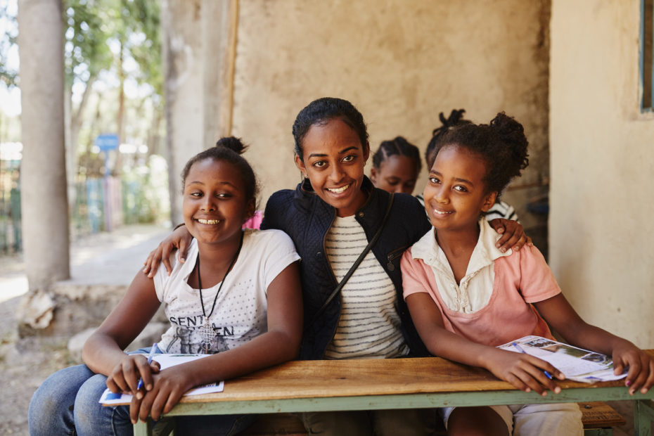 A woman sits at a table with her arms around two girls.