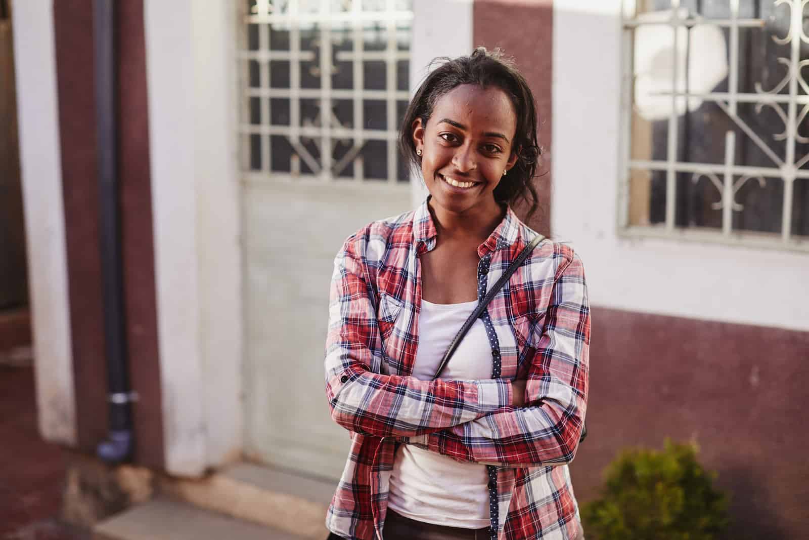 A woman in a plaid shirt crosses her arms and smiles. 