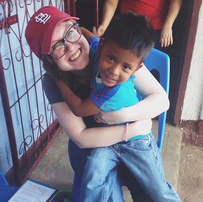 A girl in a red hat hugs a young boy as they sit in a chair.