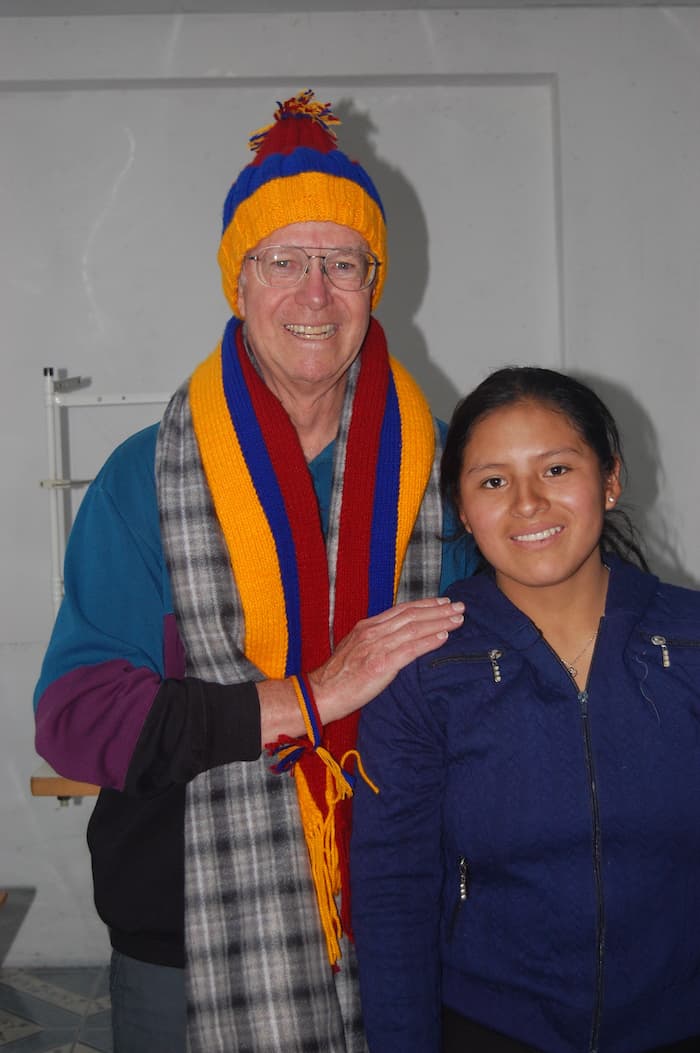 an older man wearing a colorful scarf and hat poses with a young man.