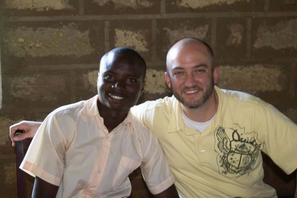 A man in a yellow shirt puts his arm around a young man in a peach-colored shirt. 