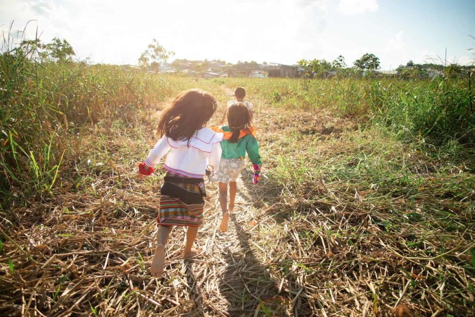 Three children run in a field wearing traditional Peruvian clothing.