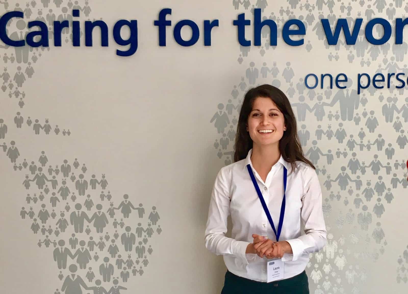 A woman stands in front of a wall that says "Caring for the world"