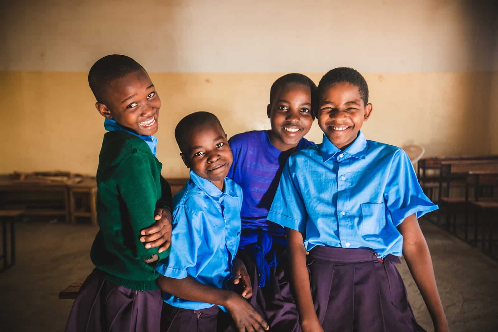 Four young Tanzanian girls wearing school uniforms smile at the camera. 
