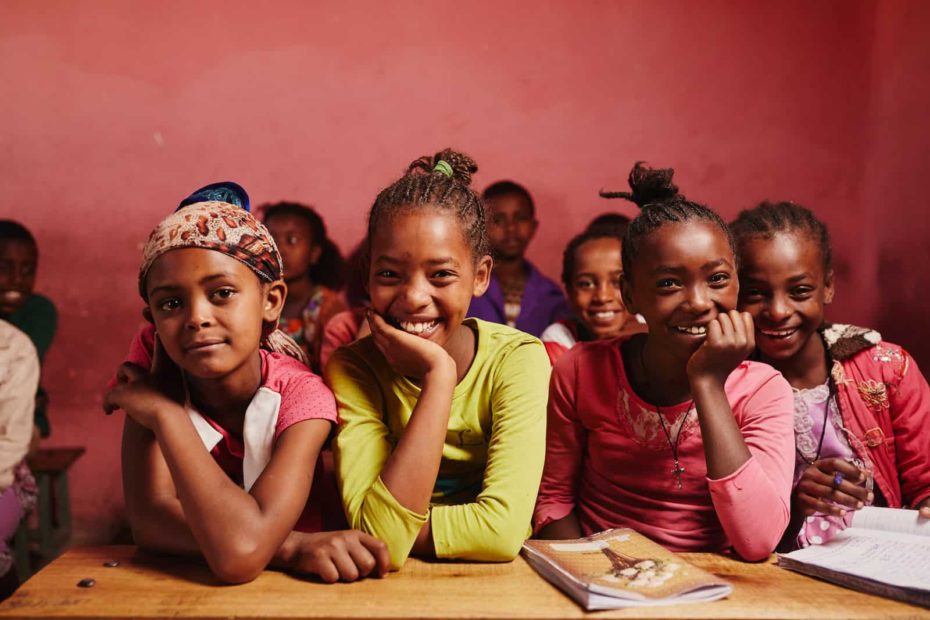 A group of girls sit in a classroom with a pink wall behind them.