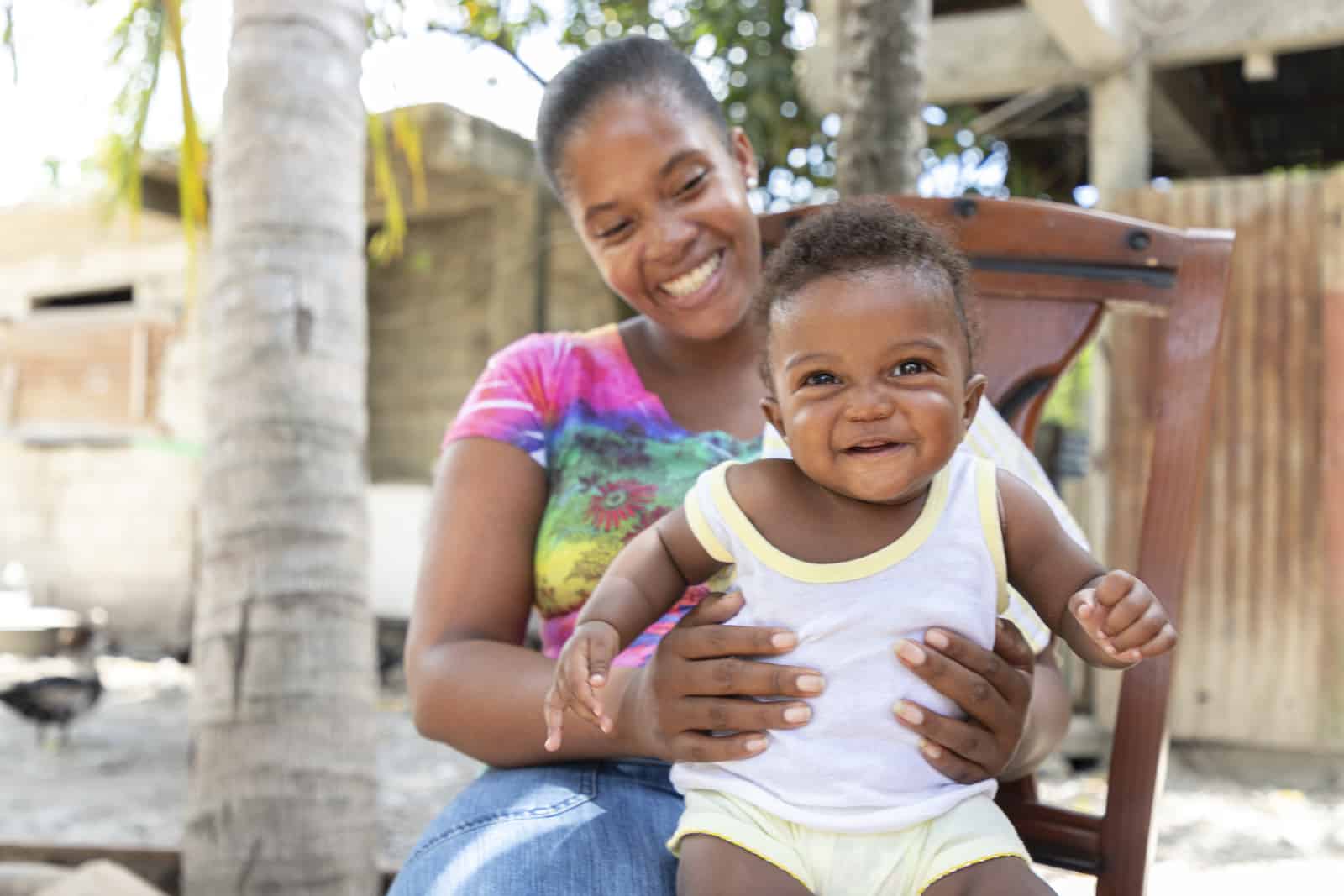 A woman holds a baby in a white shirt on her lap. 