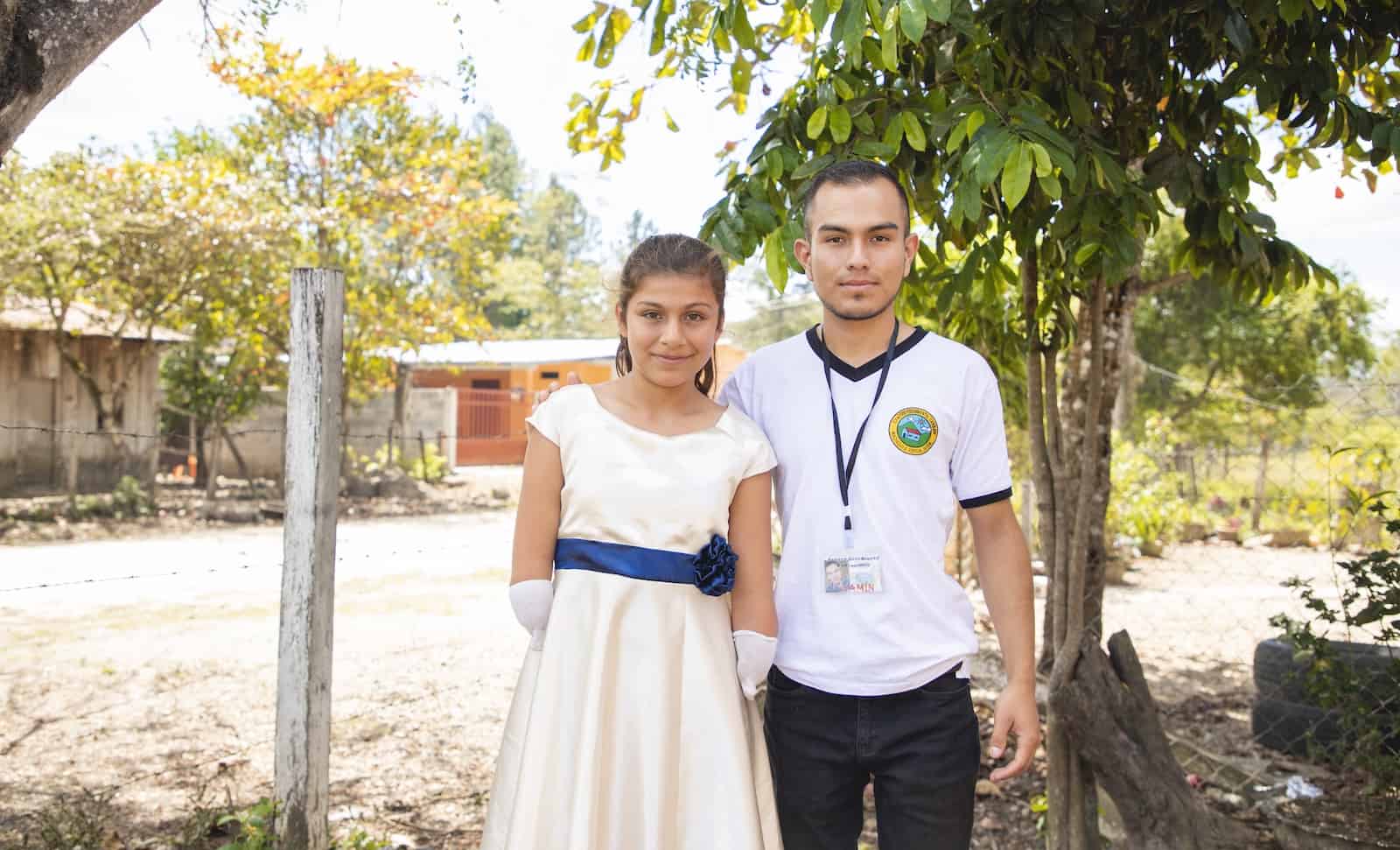 A young man and a girl with limb difference stand outside in front of a tree. 
