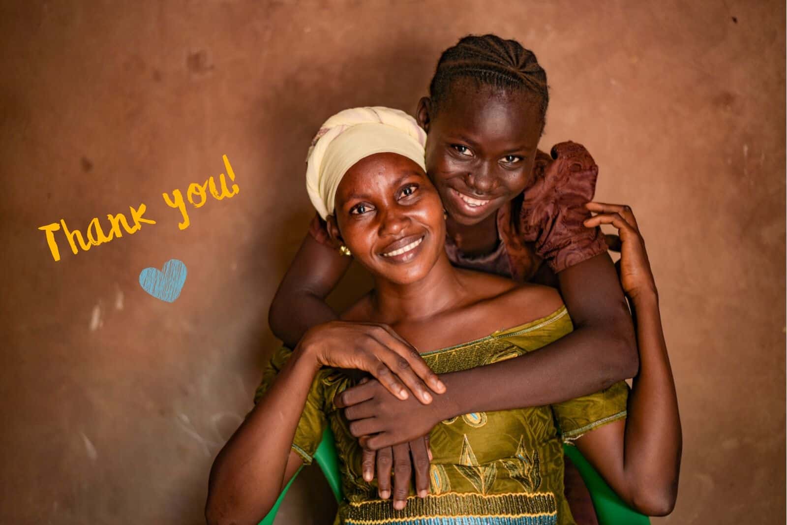 A girl in a brown dress puts her arms around a woman in a green dress and yellow turban, smiling. Text: "Thank You!"