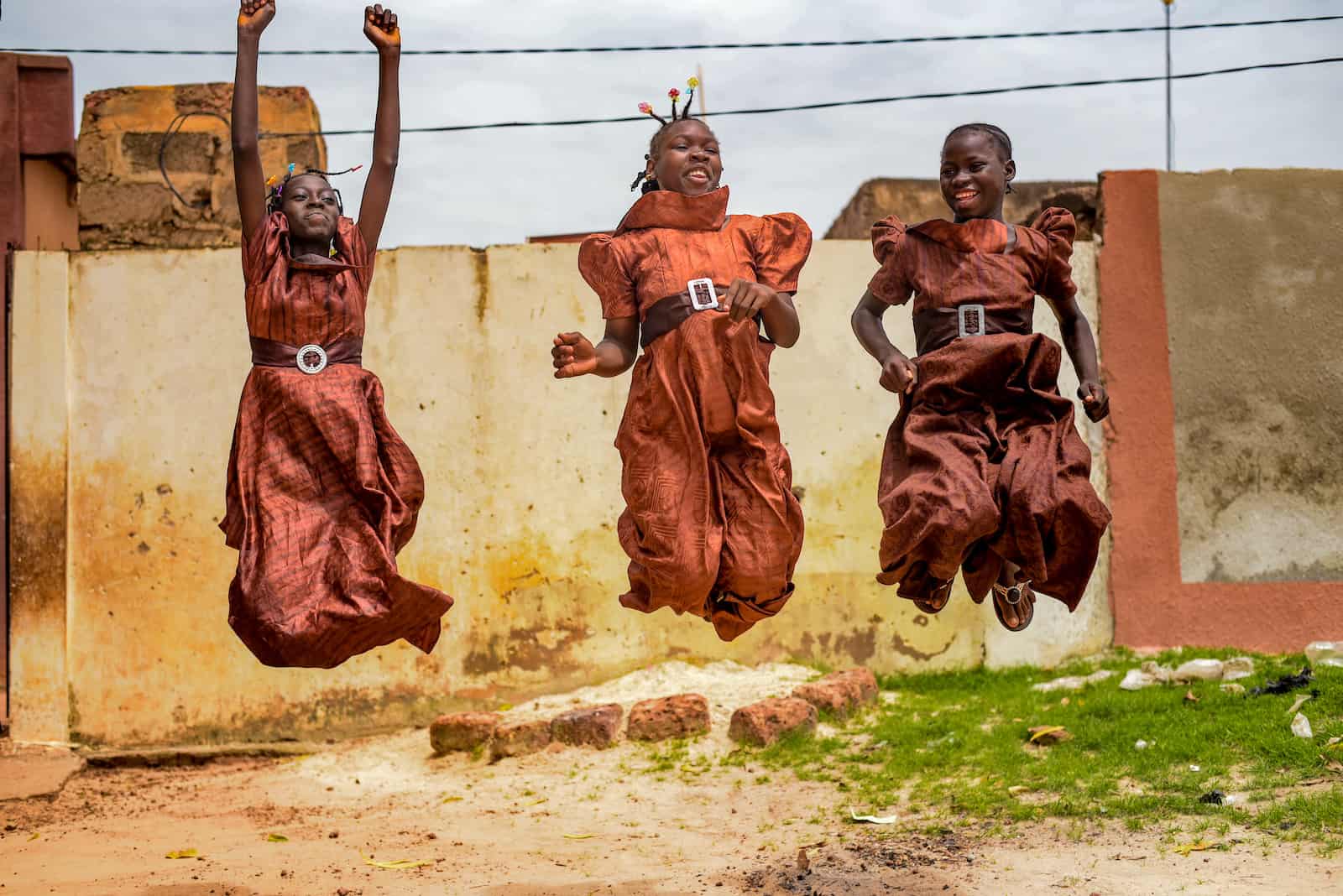 Three girls wearing brown dresses jump in the air, smiling.