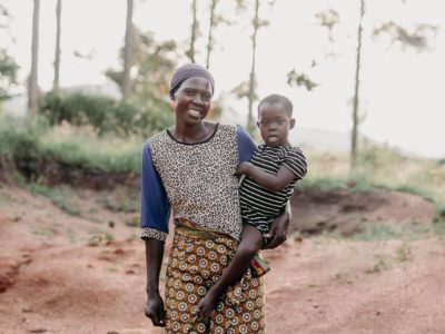 A woman holds a girl on her hip, standing on a dirt road.