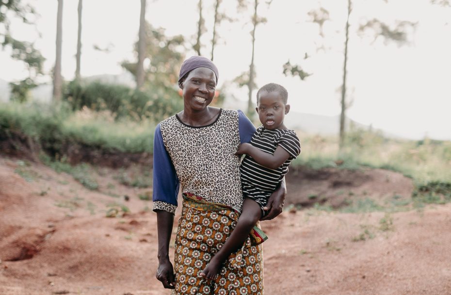 A woman holds a girl on her hip, standing on a dirt road.