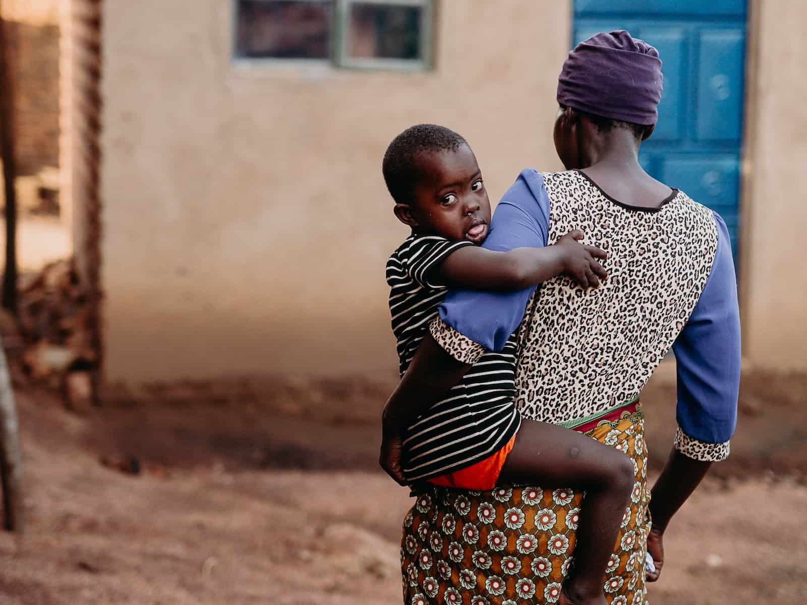 A woman walking towards a house holds a child in her arms.