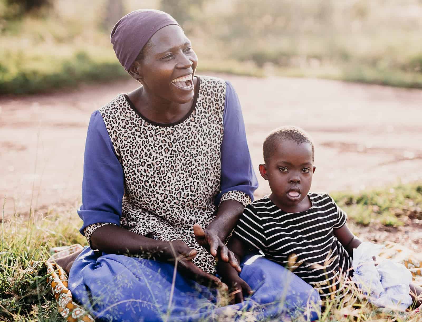 Charity Gift Heart Surgery: A woman sits on the ground, smiling, with a girl sitting next to her.