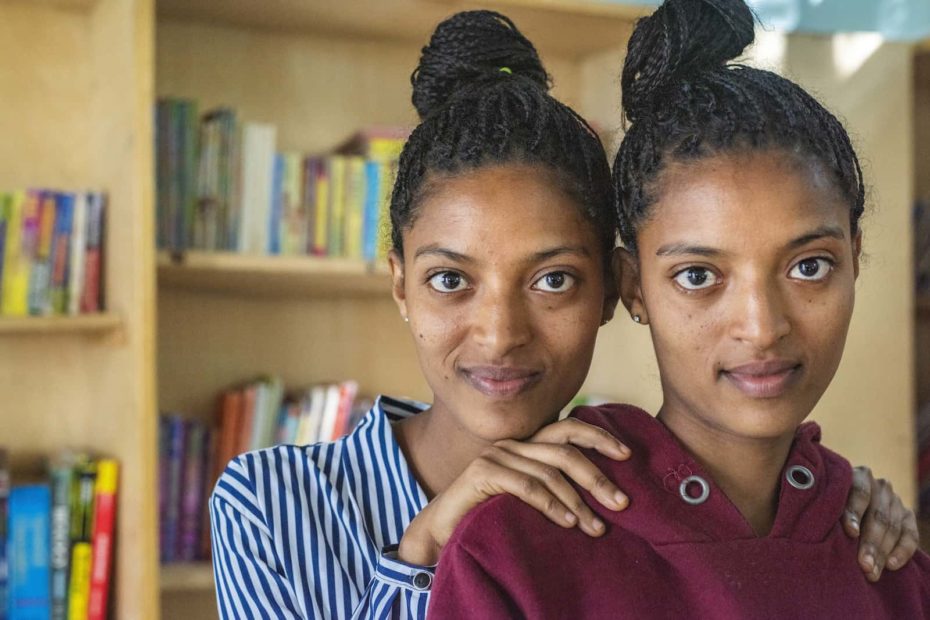 One girl stands behind another girl with her hands on her shoulders.