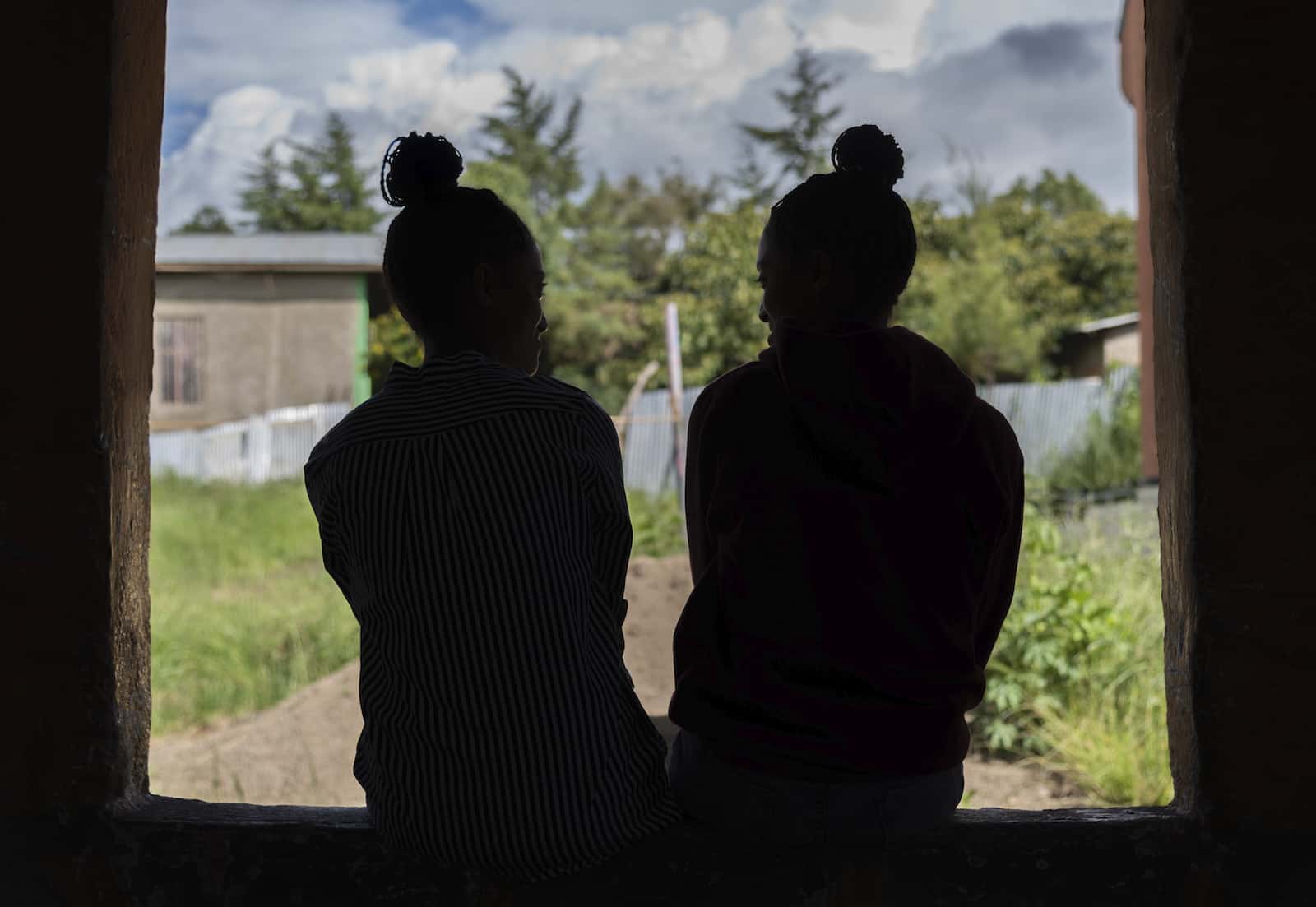 An orphan story: A silhouette from behind of two girls sitting in a window.