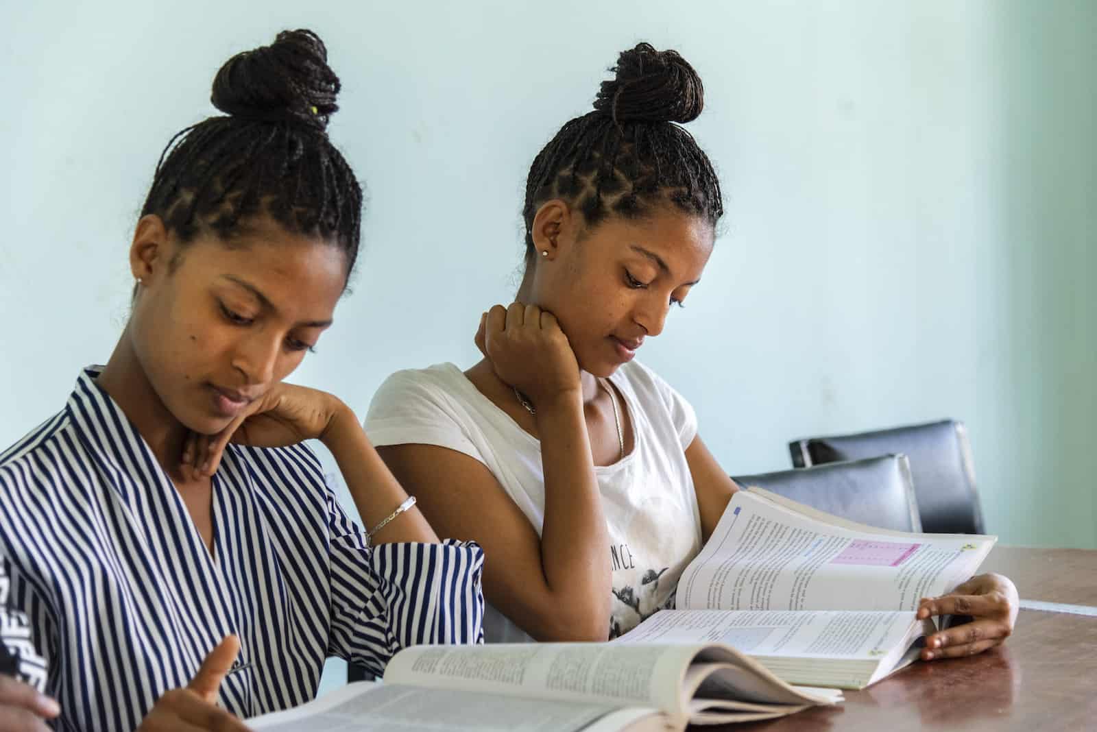 Two teenage girls sit at a desk, reading.