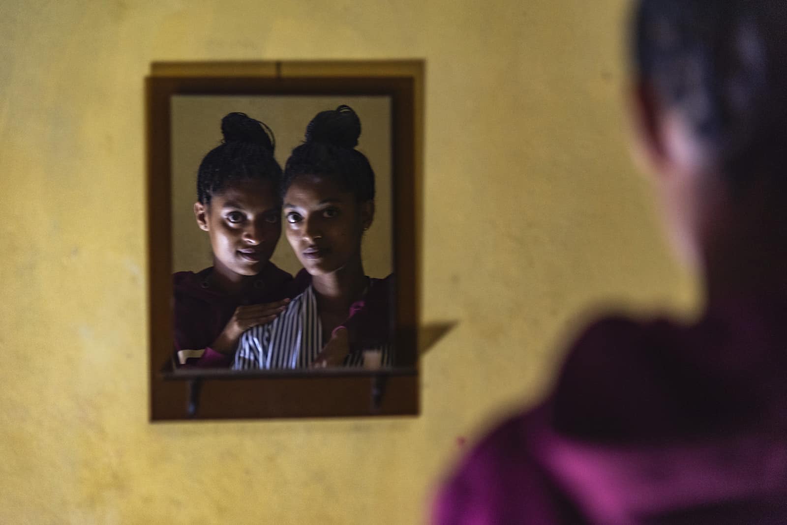 An orphan story: The mirror reflection of two teenage girls looking in the mirror.