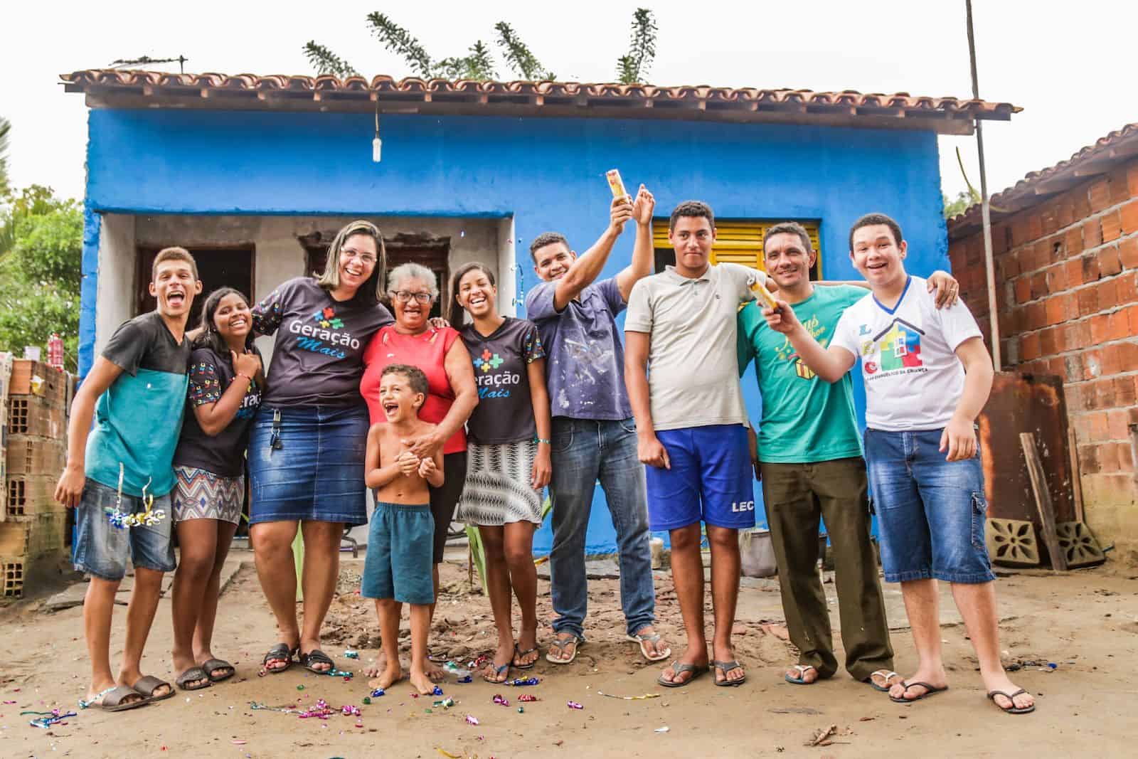 A group of teens stand in front of a newly built house with a grandmother.