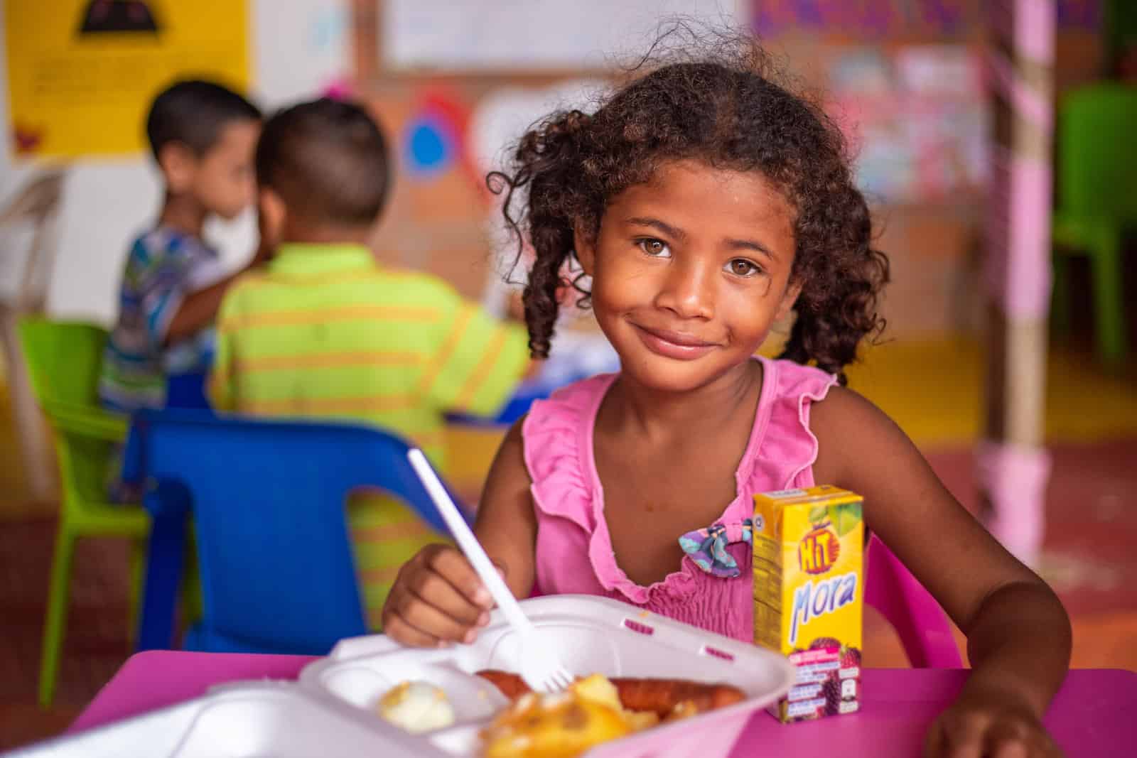 A young girl sits in front of a plate of food. 