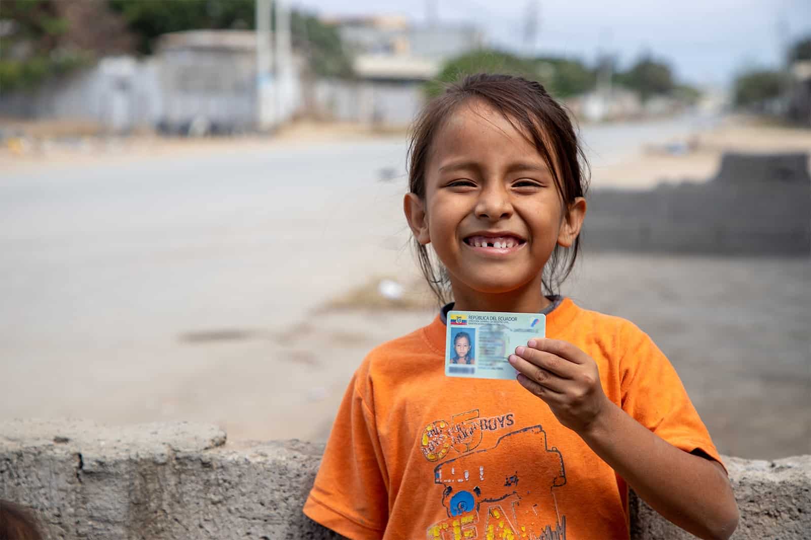 A girl in an orange shirt holds up an identification card. 