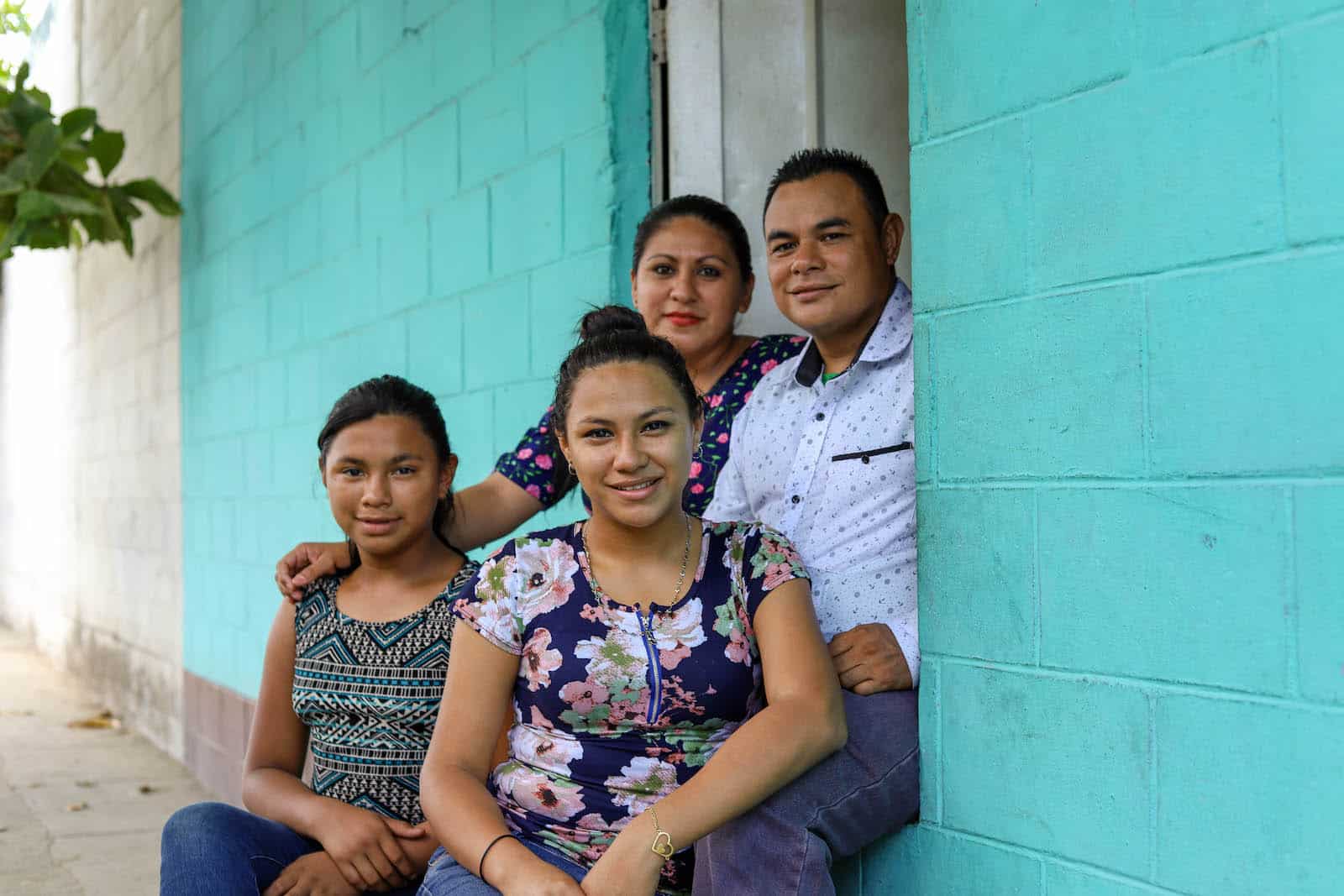 A family of four sits on the doorstep of a turquoise painted home.
