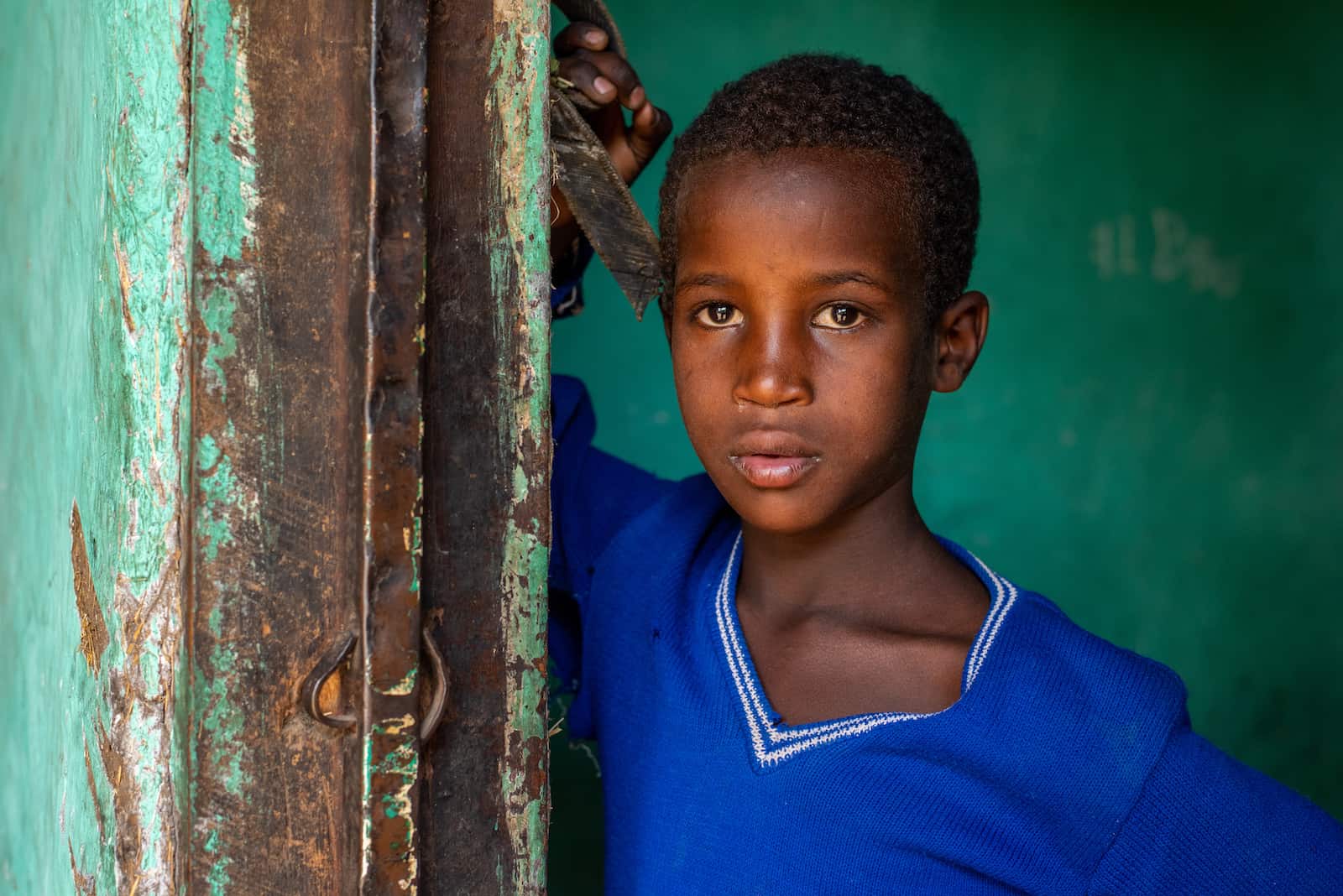 A boy in a blue shirt stands next to a green door. 