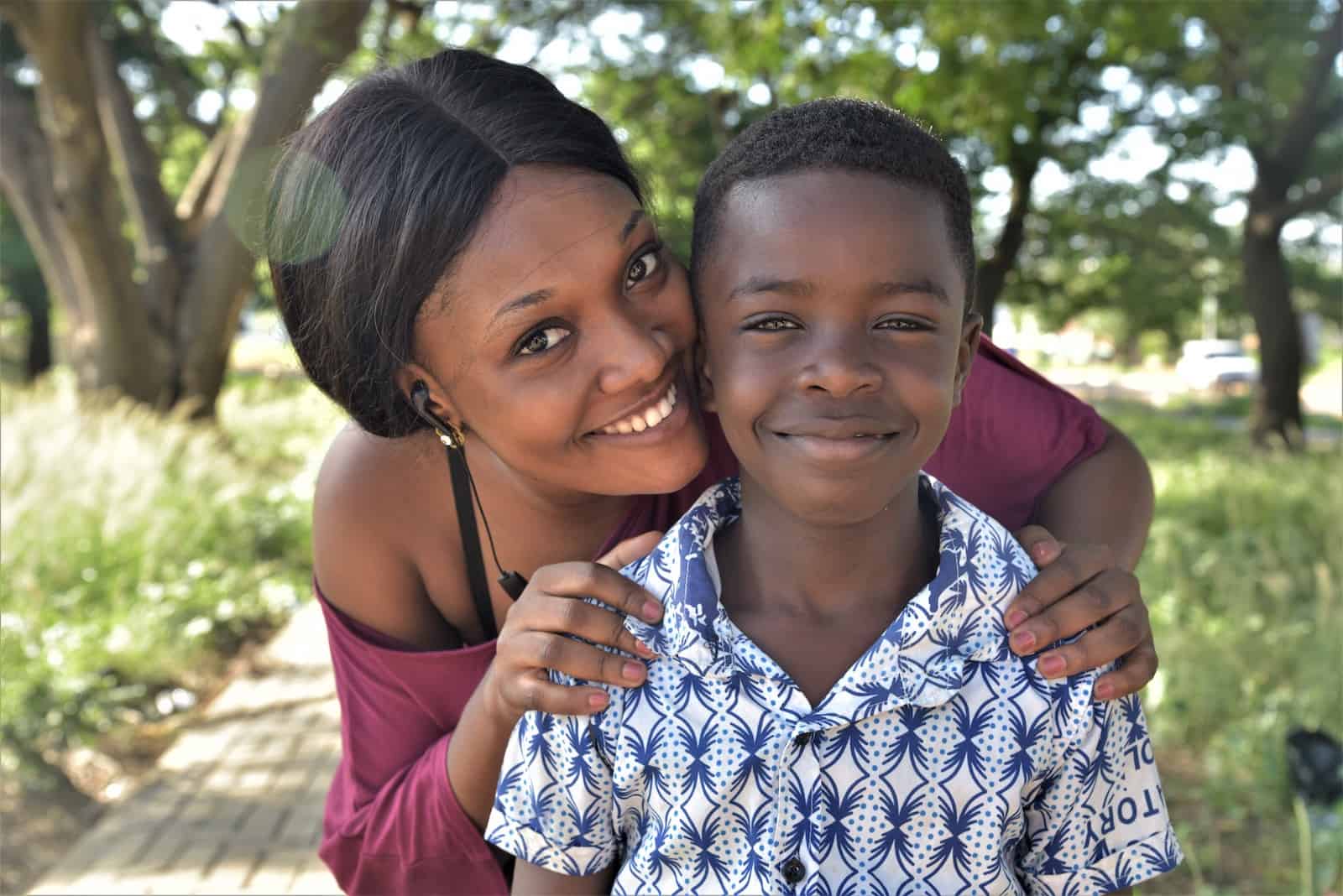 A woman in a maroon shirt hugs a boy in a white shirt. 