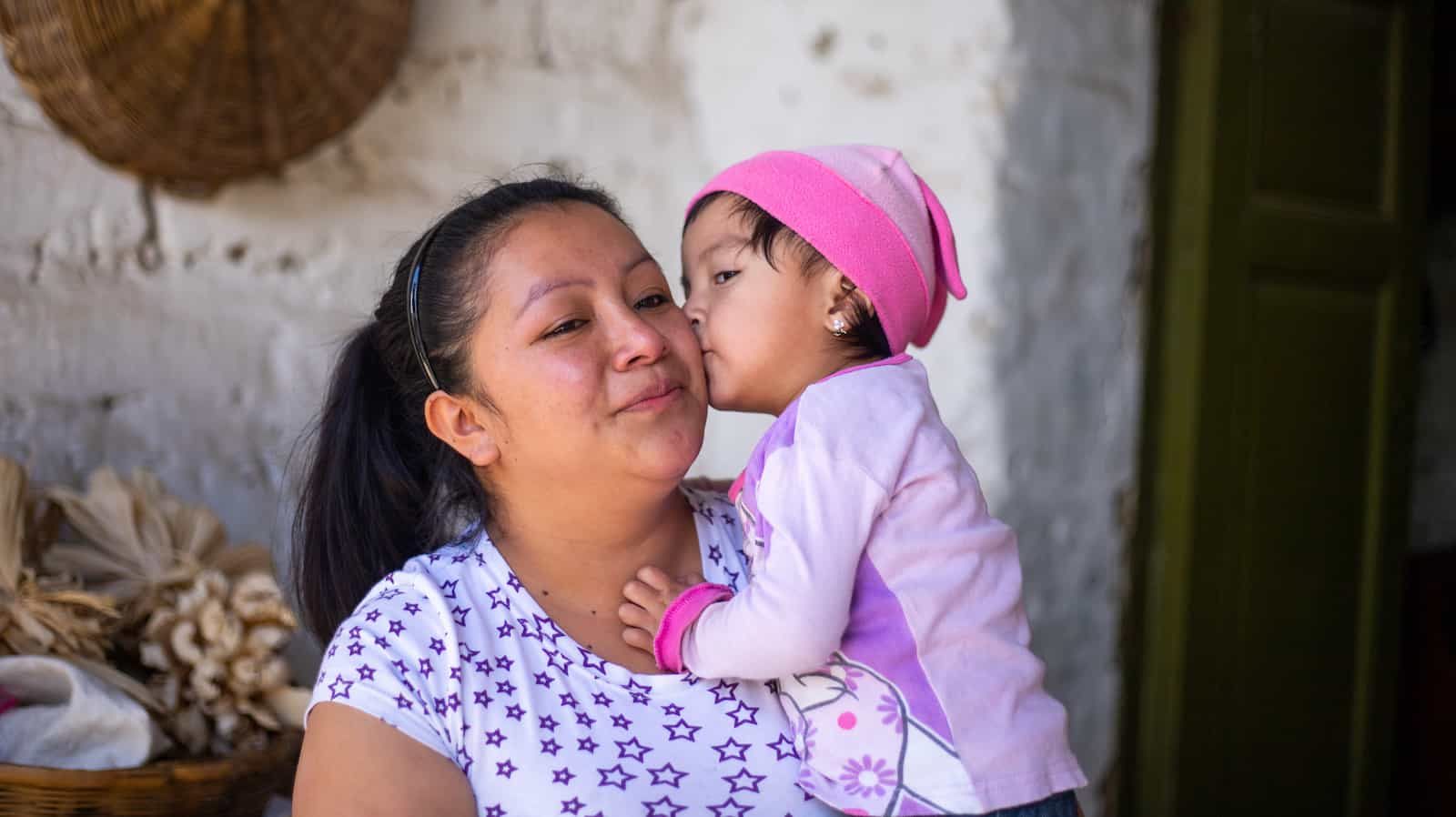 A little girl kisses her mom on the cheek.