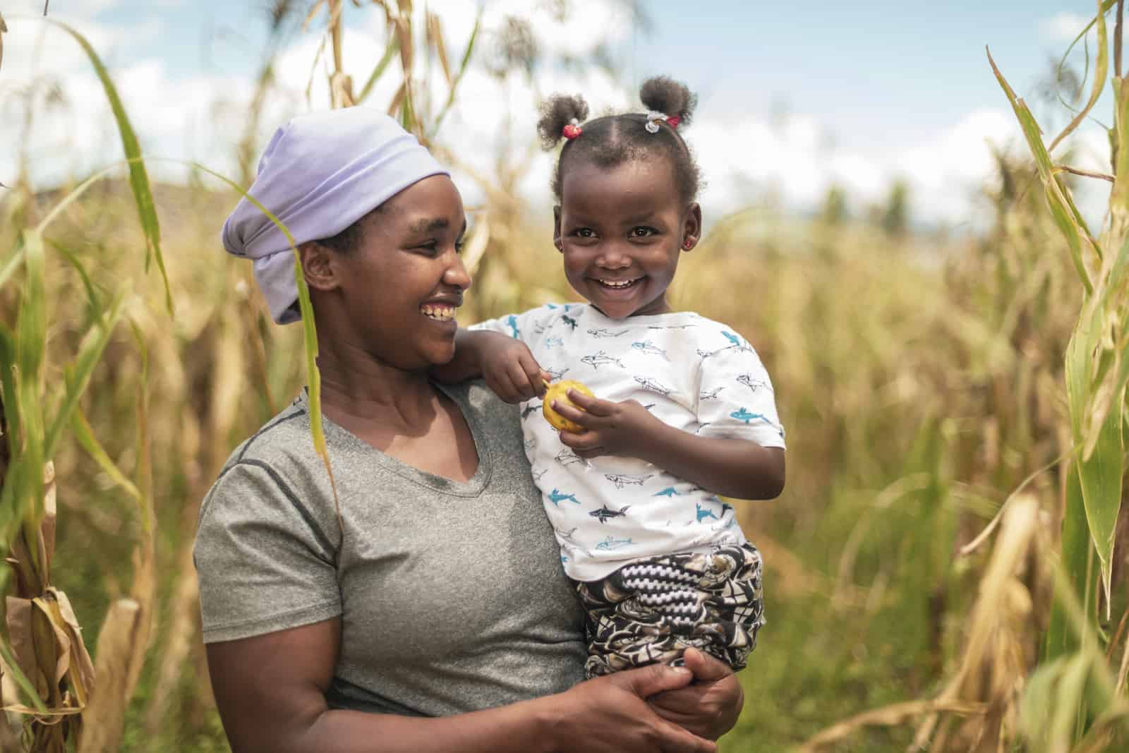 A woman in a cornfield holds a toddler. 