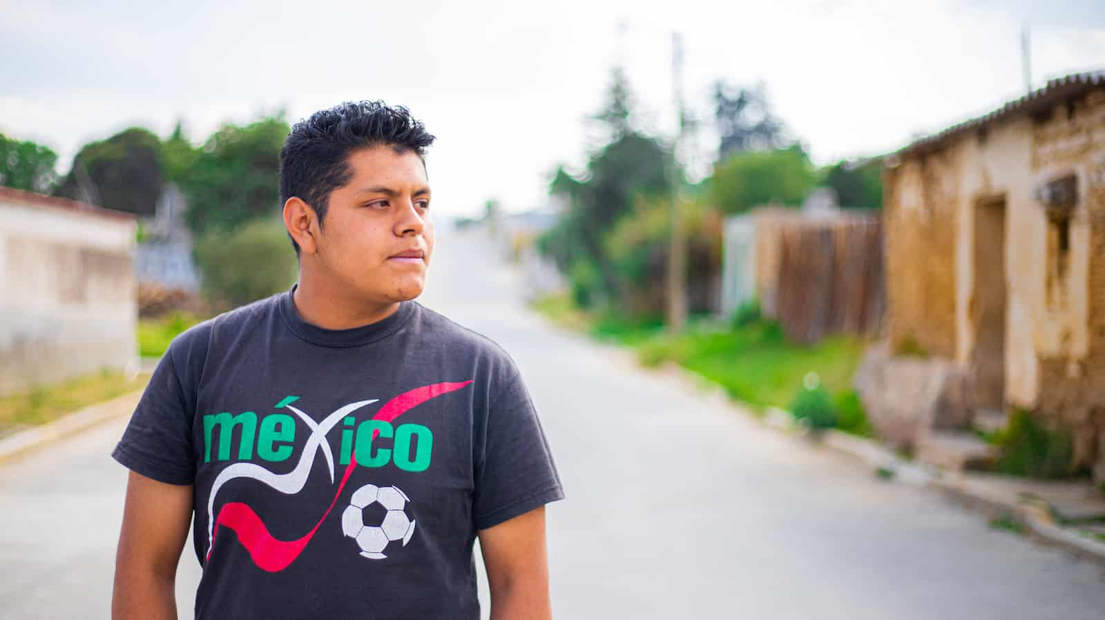 A young man in a black shirt on a paved street looks to the side. 