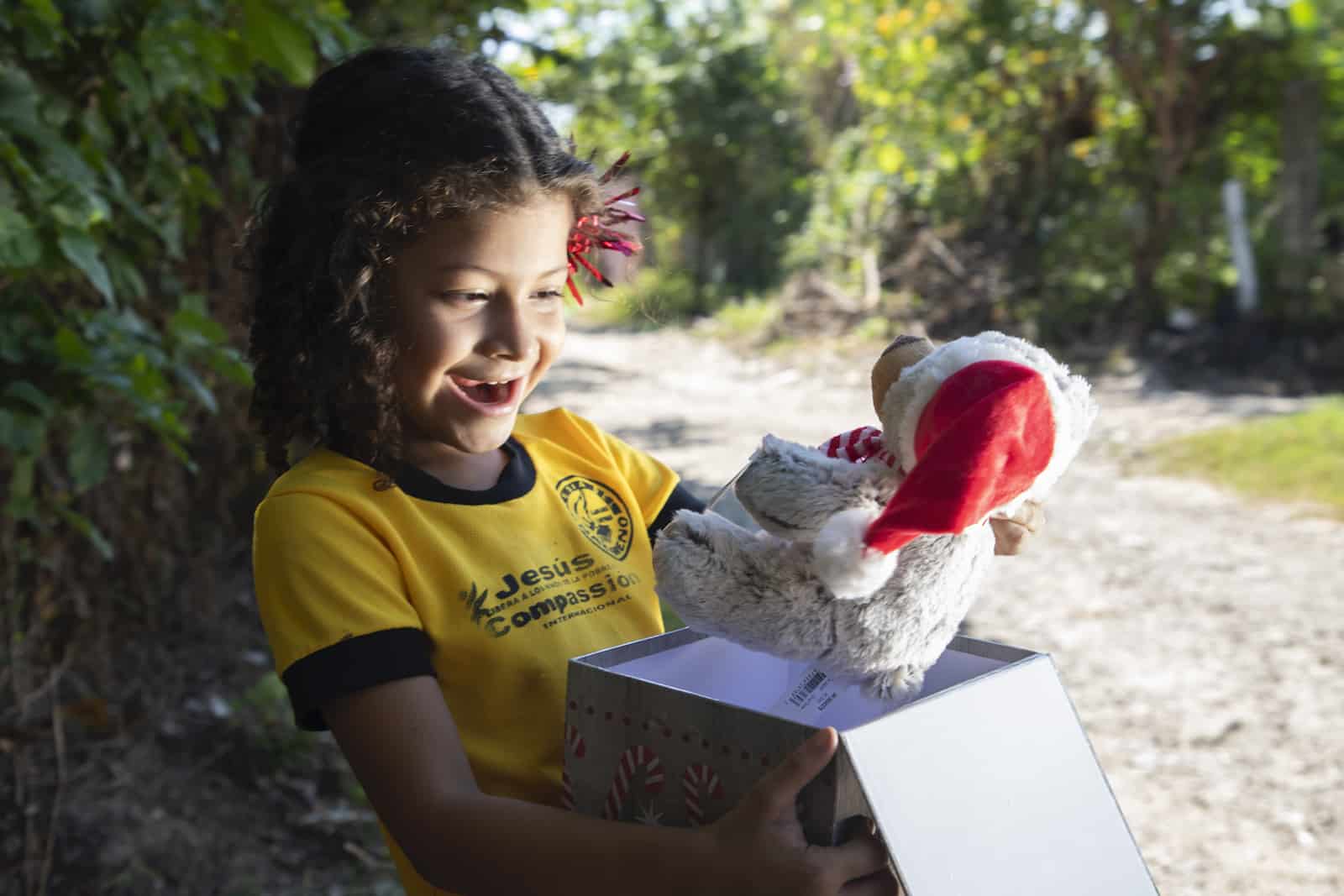 Christmas in El Salvador: A girl opens a gift with a teddy bear in it. 