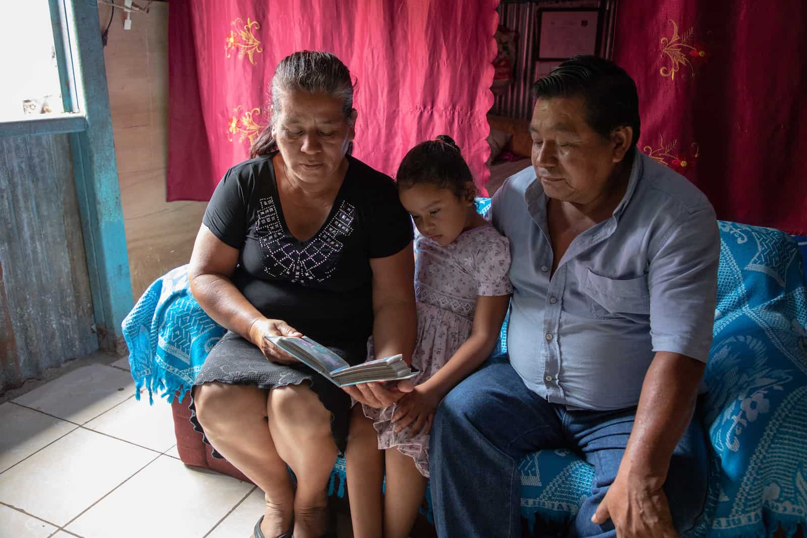 A man, woman and girl sit on a bed, looking at a photo album.