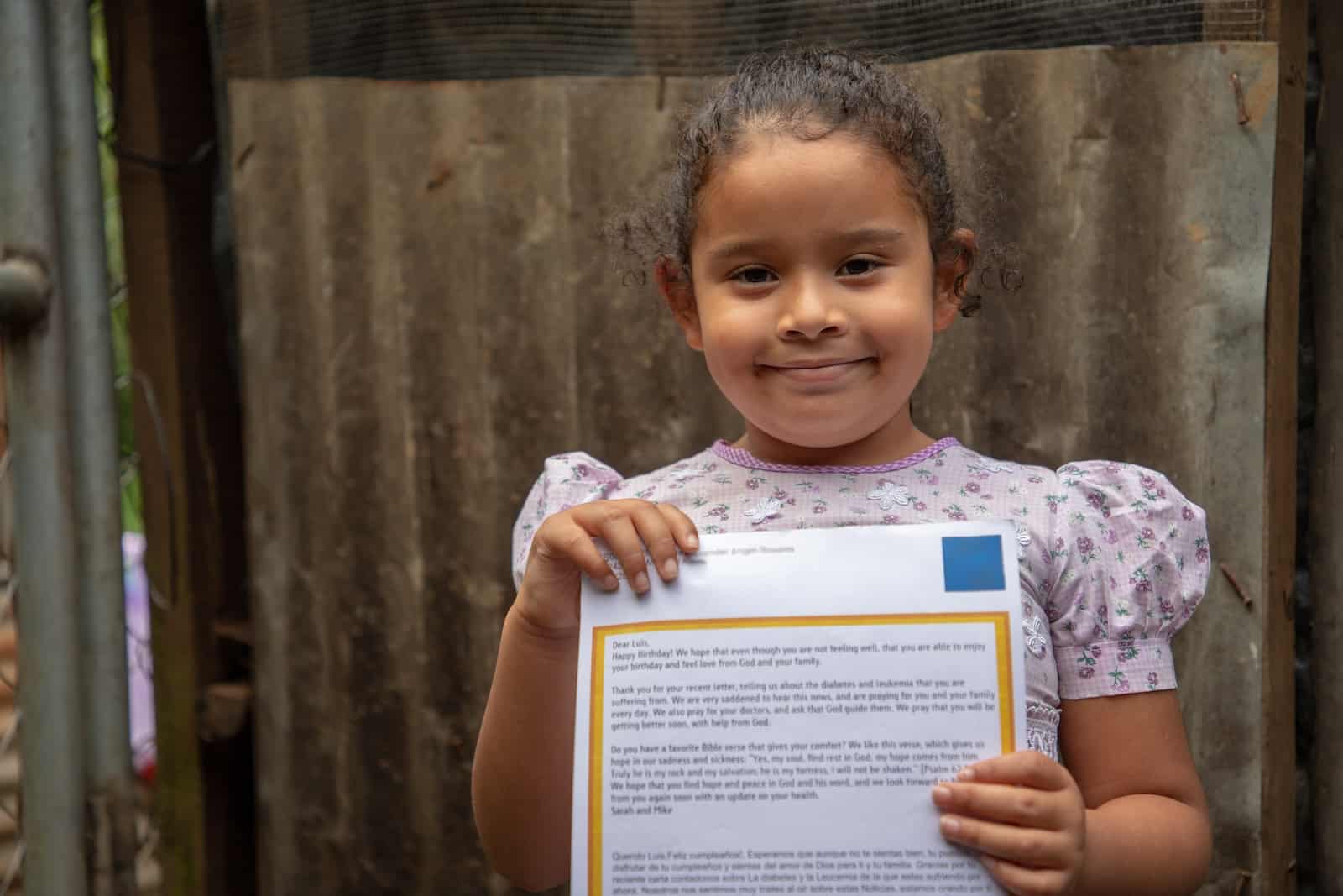 A girl in a pink dress holds a letter. 